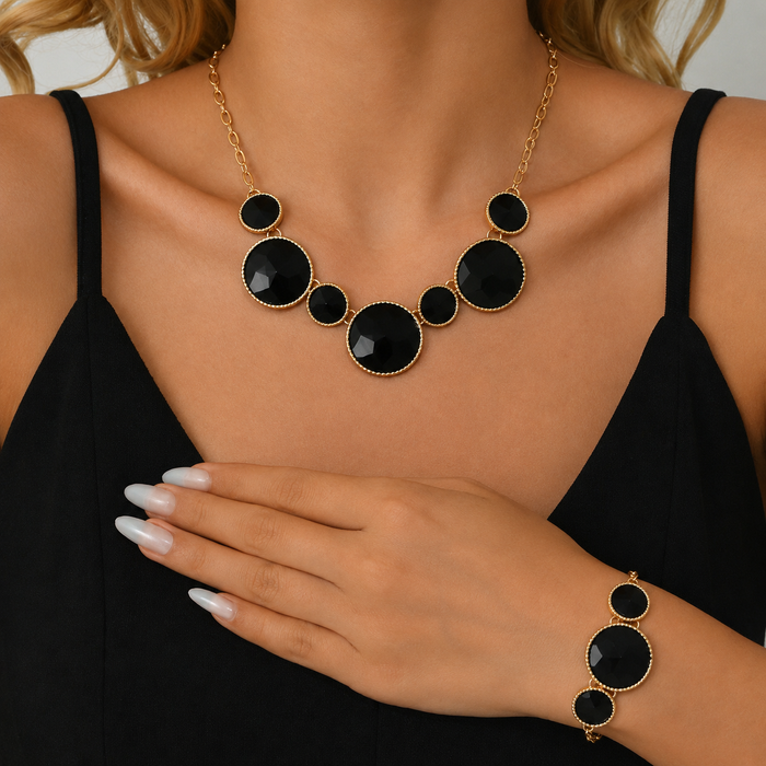 A gold-toned statement necklace and matching bracelet set with large black oval stones, shown on a model wearing a black top.