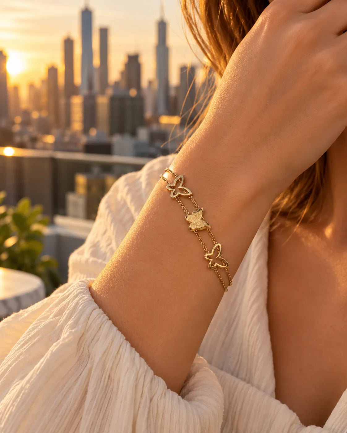 Wrist wearing the gold butterfly bracelet against a city skyline at sunset