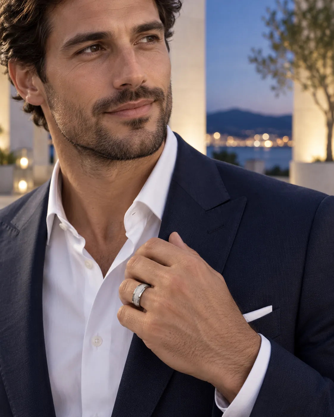 Man in a navy suit wearing the silver band ring at dusk