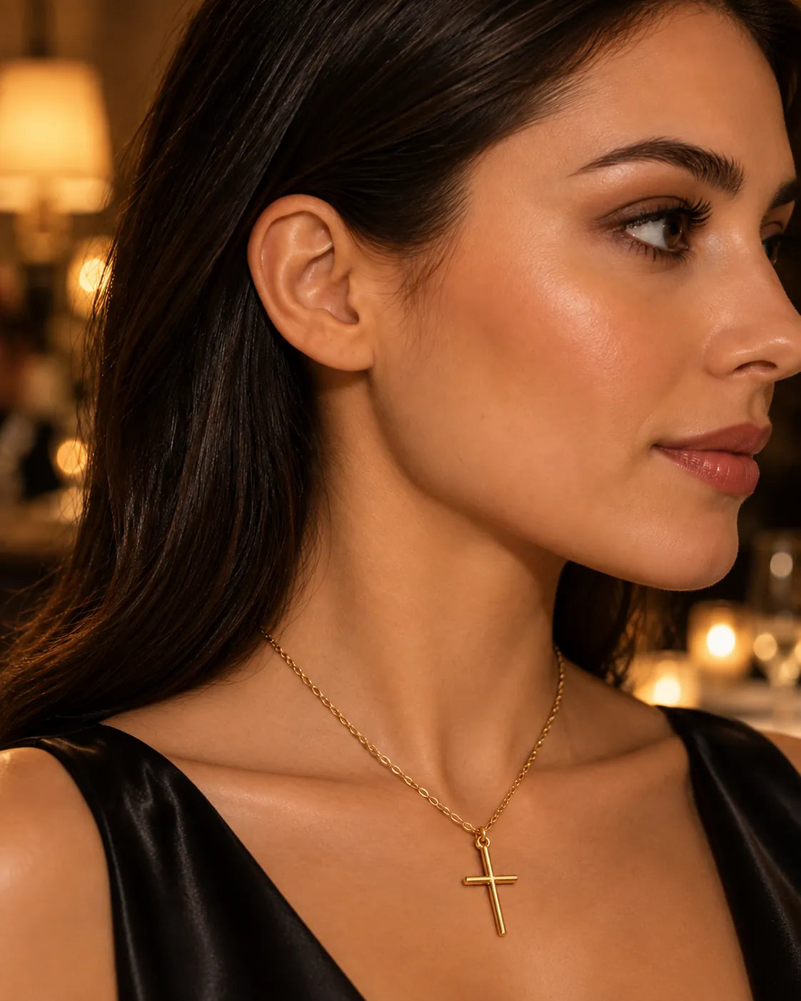 Model in a black top wearing the minimal gold cross necklace in warm light