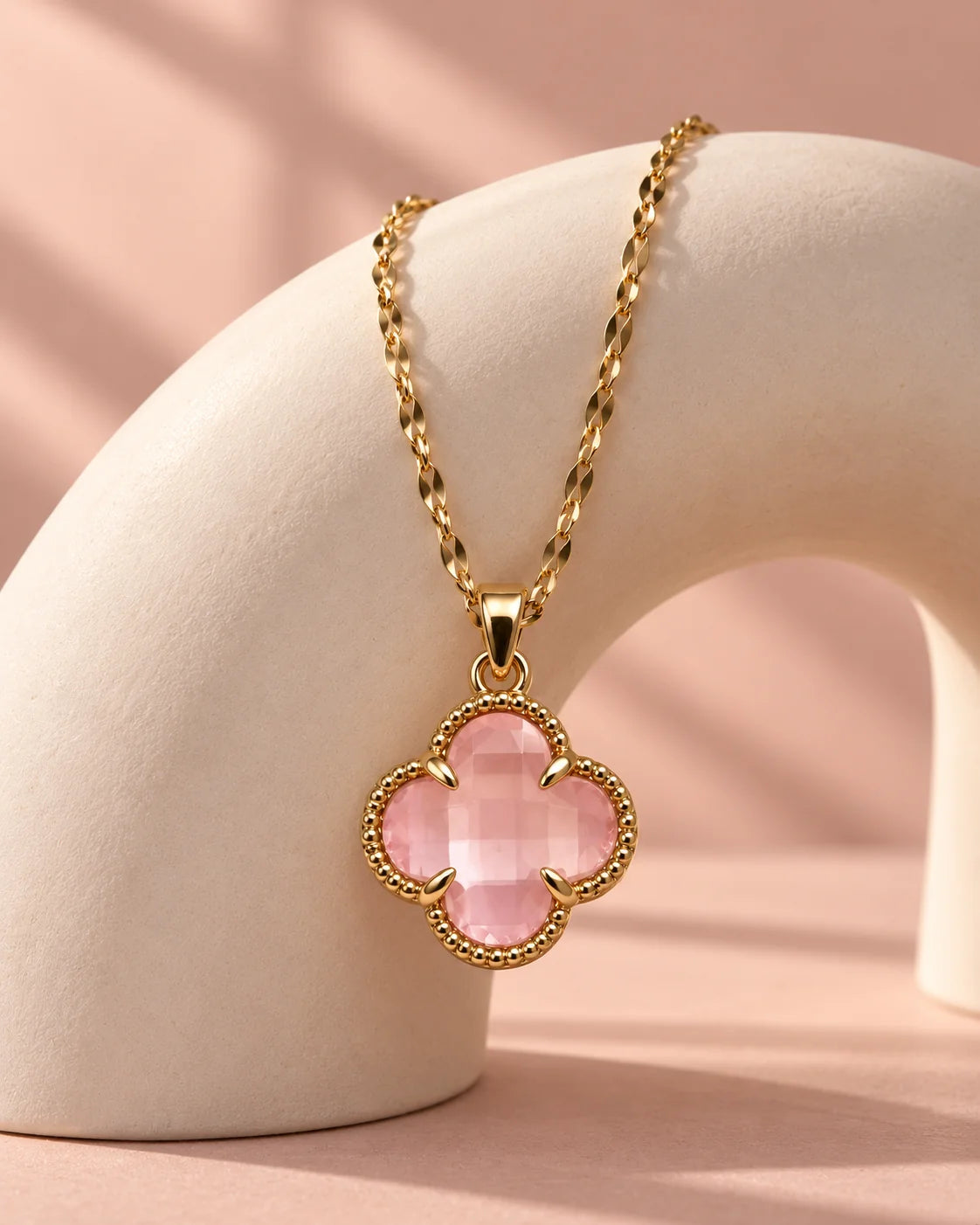 Fortuna baby pink clover necklace draped over an ivory arch against a blush backdrop