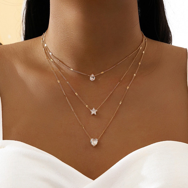 Layered gold necklaces with heart and star pendants on a mannequin.