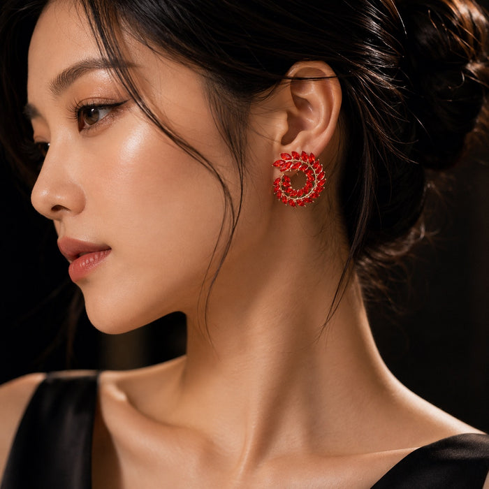 A close-up side profile of a woman wearing a red spiral-shaped stud earring with sparkling clear stones, set against a dark background.