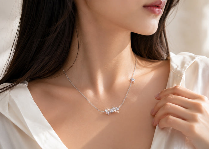 A close-up lifestyle shot of a model wearing a delicate silver necklace with a small cluster of clear crystals at the center, accented by a tiny star on the chain.