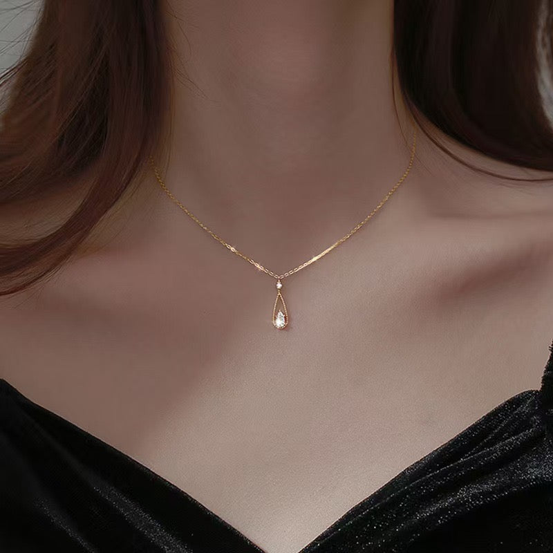 A delicate gold chain necklace with a teardrop-shaped rose gold pendant featuring a clear crystal, shown worn on a model's neck.