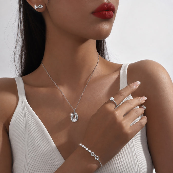 A close-up lifestyle shot of a model wearing a delicate silver necklace with a crescent moon pendant, matching silver stud earrings, a silver ring, and a silver bracelet, paired with a white ribbed tank top.