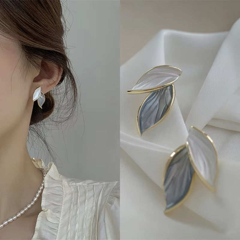 Leaf-shaped earrings with gold accents worn by a person, displayed on a white fabric background.