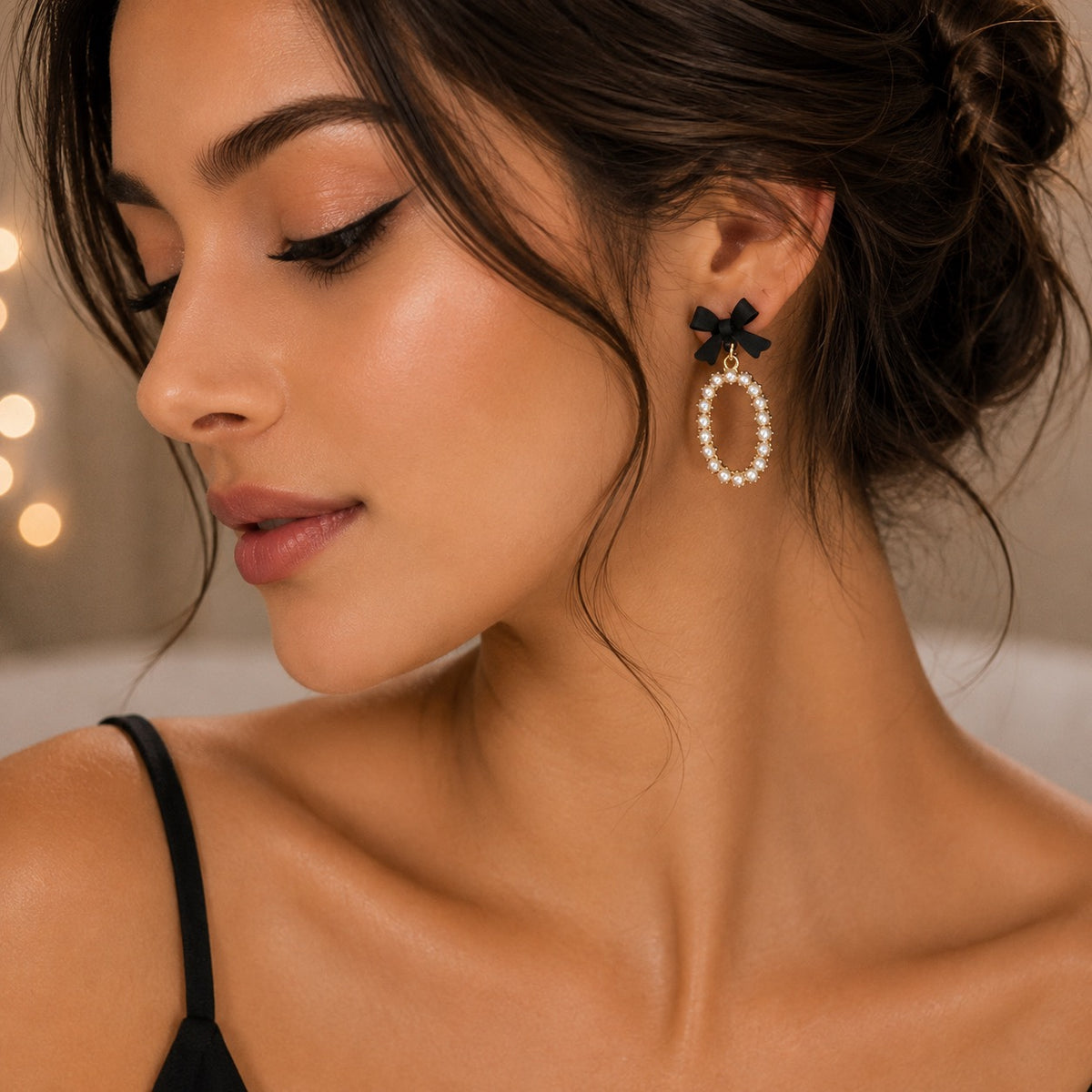 A close-up of a woman wearing a dangling earring with a black bow at the top and a circular drop made of white faux pearls outlined in gold.