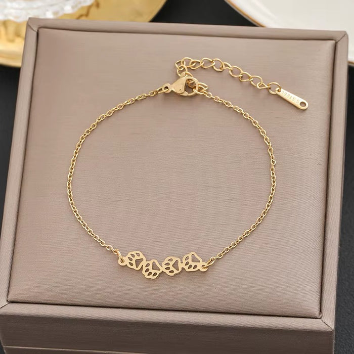 A delicate gold chain bracelet with five interlocking heart-shaped charms, displayed inside a textured taupe jewelry box.