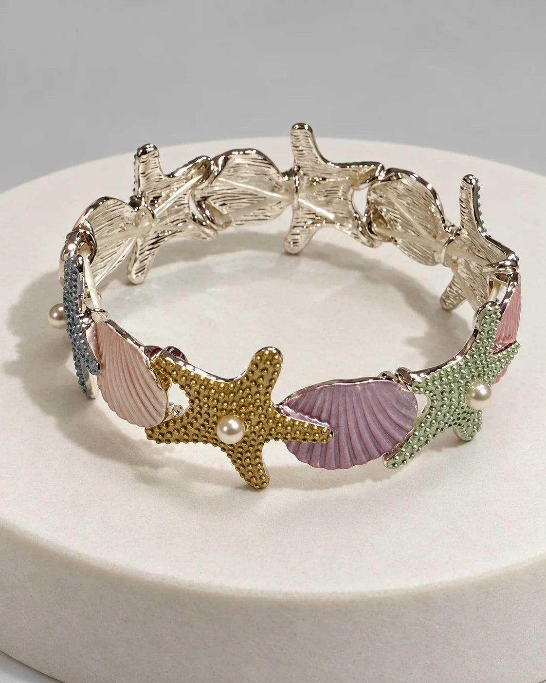 Marina pastel enamel starfish and shell bracelet in silver tone on a white stone plinth