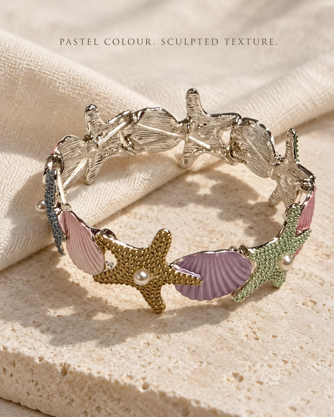 Pastel coastal shell and starfish bracelet resting on sandstone and linen