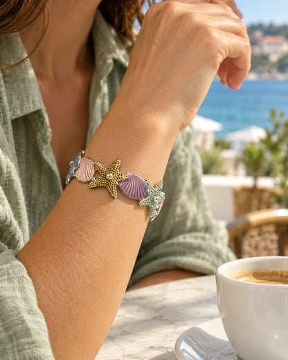 Woman at a seaside café wearing the pastel enamel starfish and shell bracelet