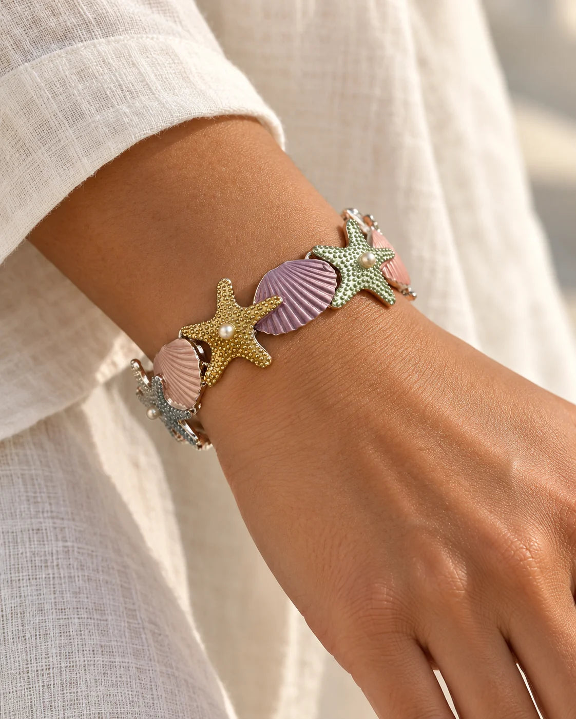 Pastel starfish and shell bracelet worn on the wrist with a linen shirt
