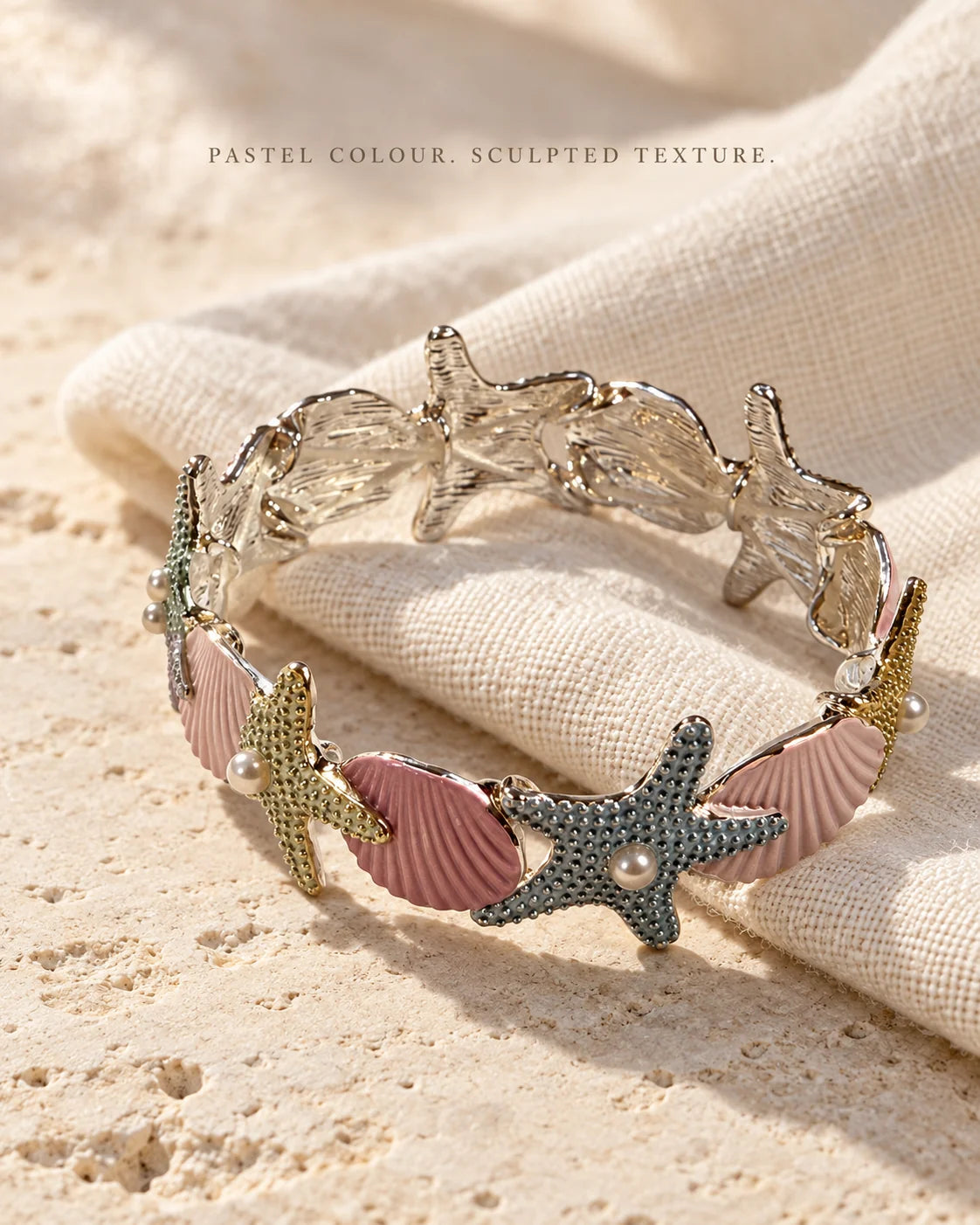 Pastel enamel starfish bracelet on cream linen showing sculpted texture