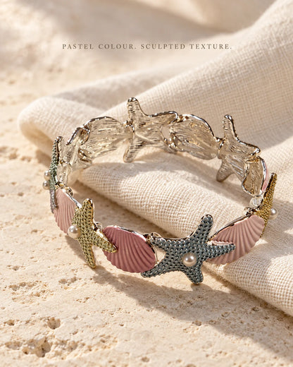Pastel enamel starfish bracelet on cream linen showing sculpted texture