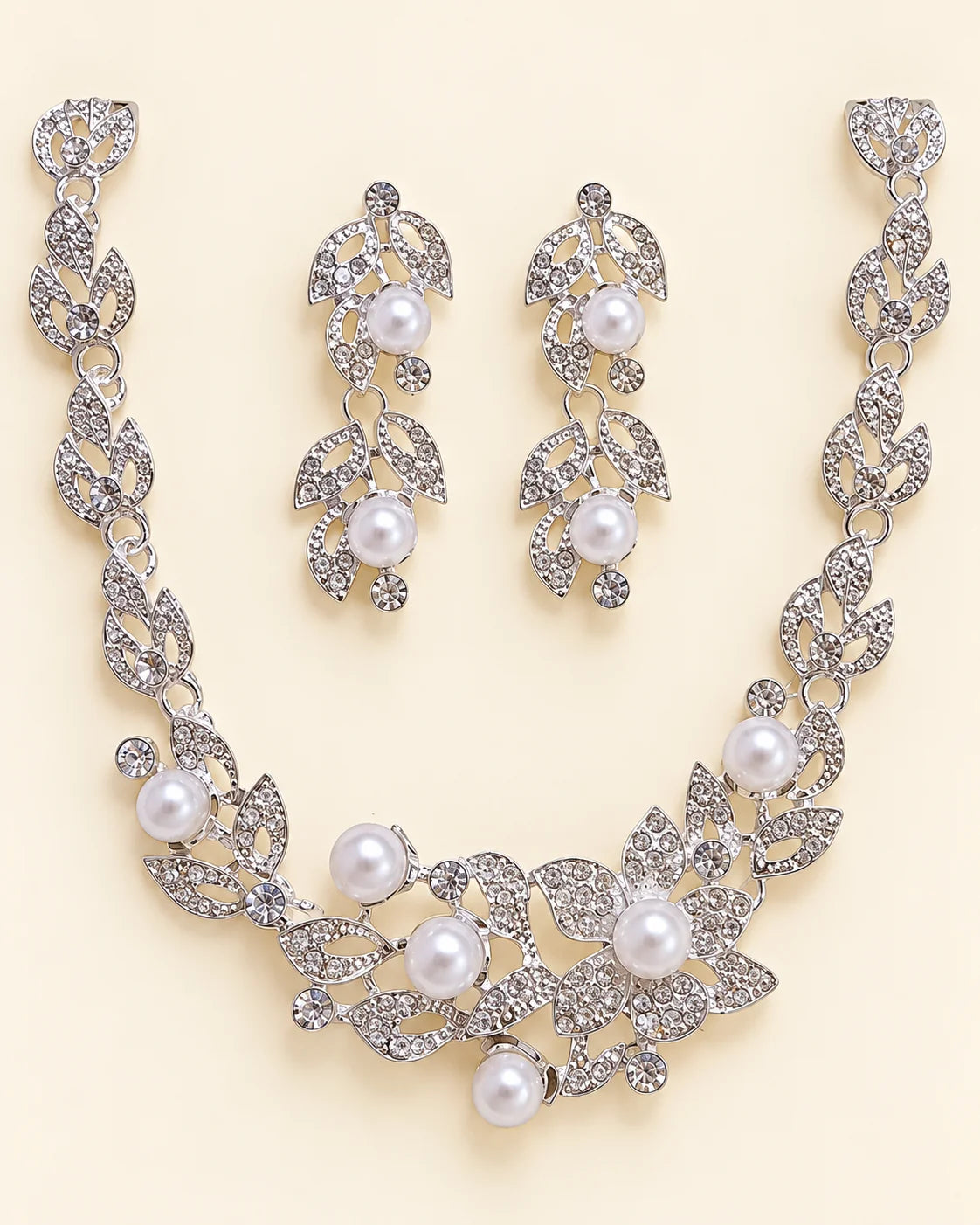 Ivy silver leaf and pearl bridal jewellery set laid flat on cream, showing the leaf vine necklace and matching pearl drop earrings