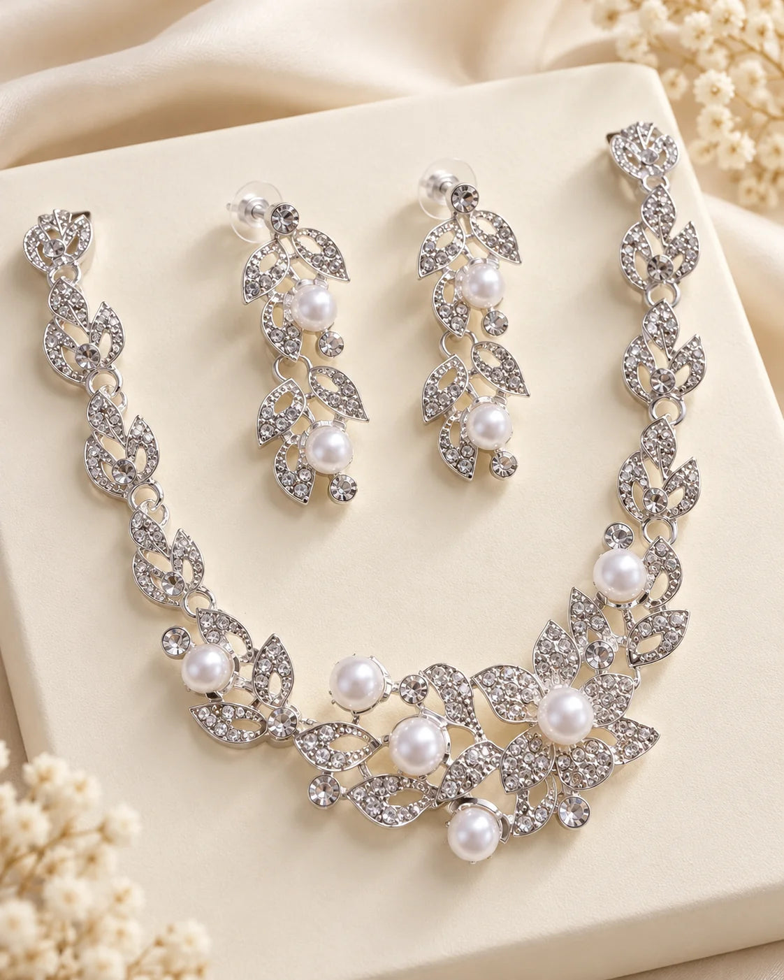 Ivy silver leaf and pearl necklace and earrings displayed on a cream stand with baby's breath flowers
