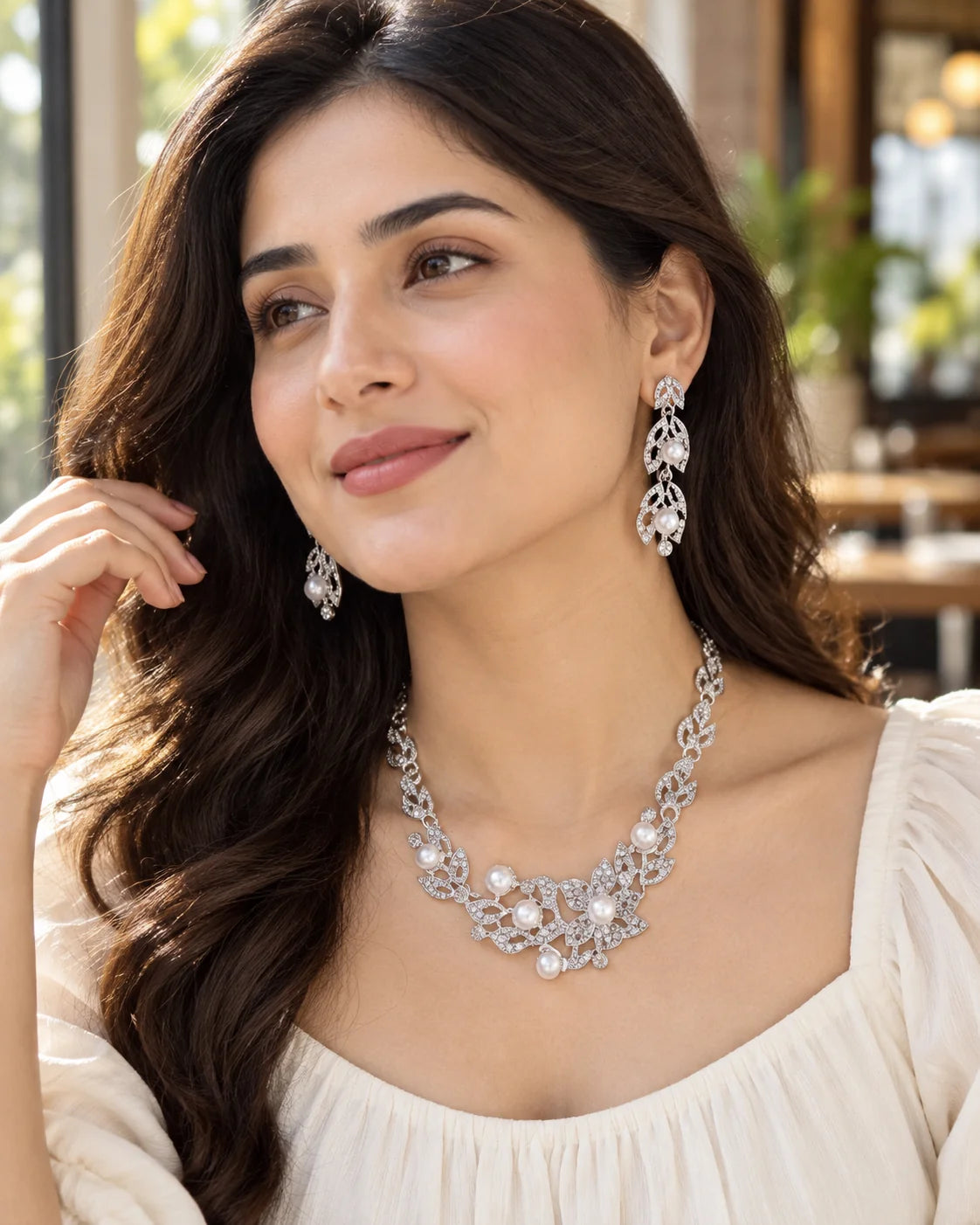 Woman in a sunlit café wearing the silver leaf and pearl necklace and drop earrings