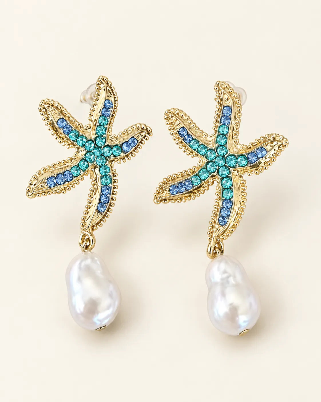 Gold starfish stud earrings with turquoise stones and pearl-look drops on a cream background
