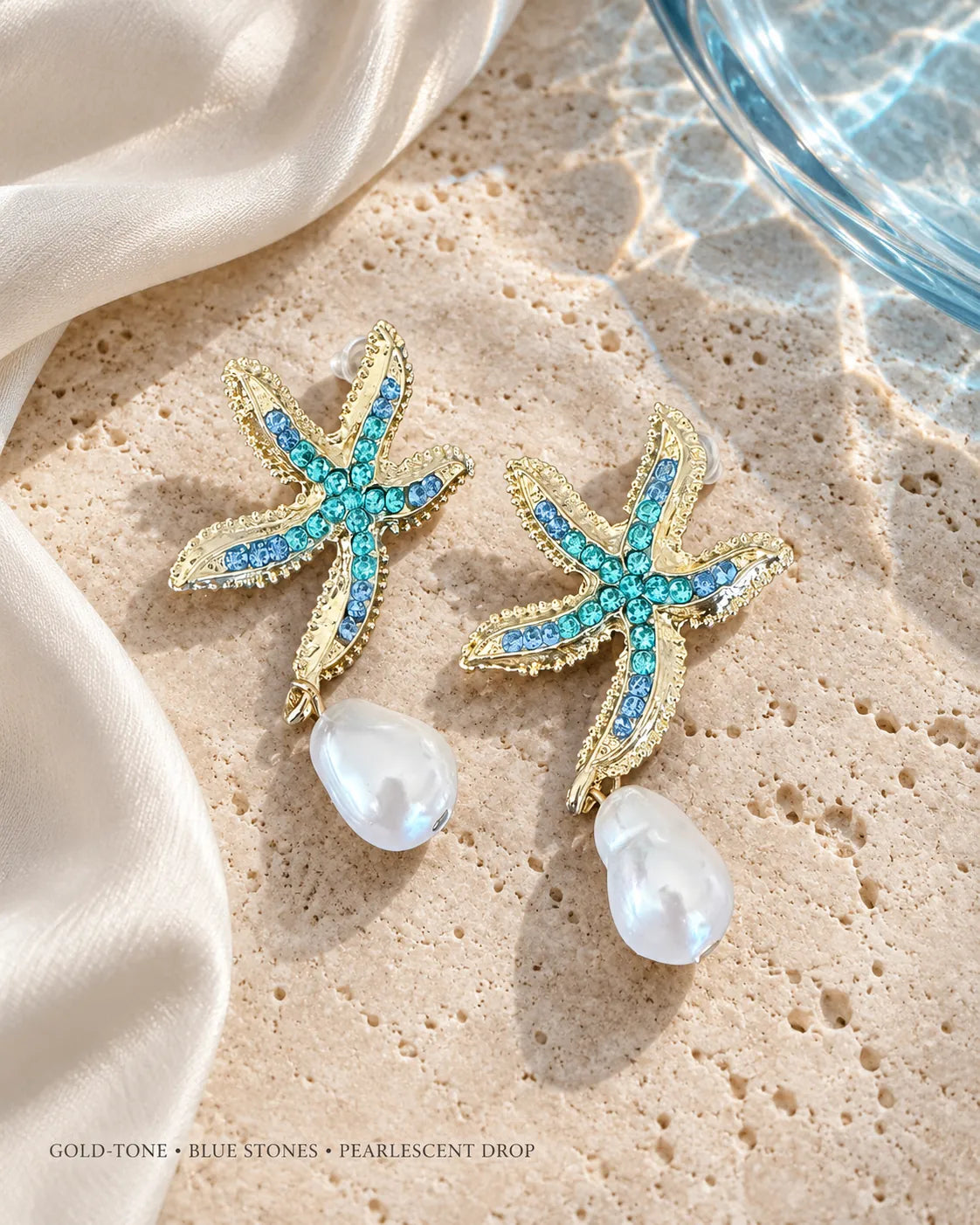 Gold starfish earrings with pearl-look drops on sand beside water