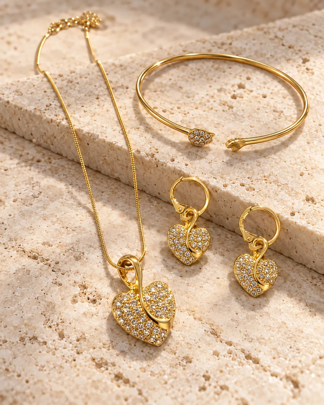 Gold pavé heart necklace, huggie earrings and cuff bangle on a stone block