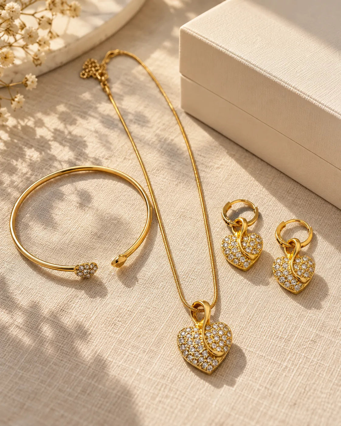 Gold-tone pavé heart jewellery set arranged on cream beside a stone block