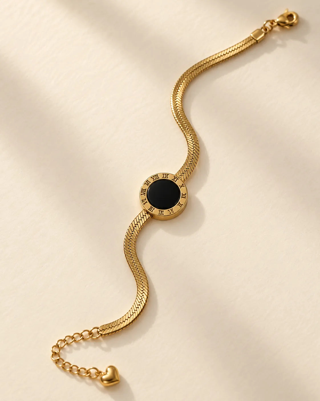 Gold flat chain bracelet with black enamel disc laid in a wave