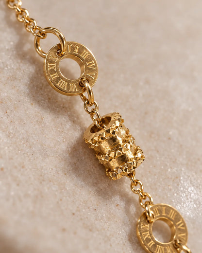 Close-up of the Roman numeral rings and textured drum bead on the gold bracelet
