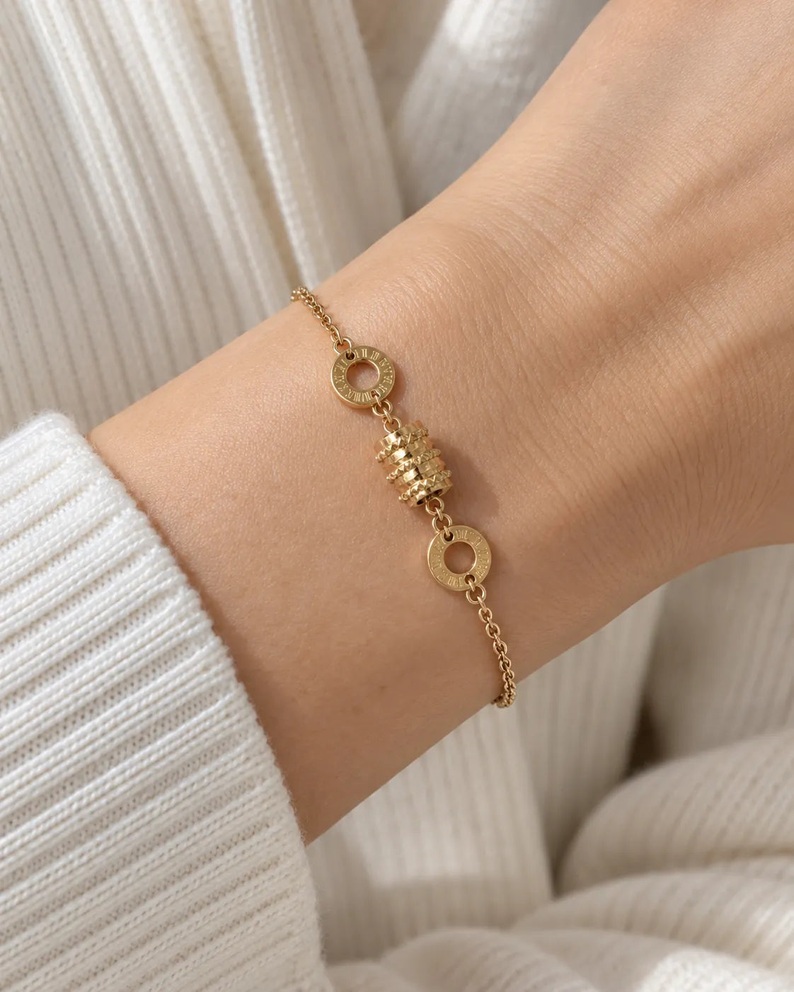 Wrist in a white knit wearing the gold drum charm bracelet