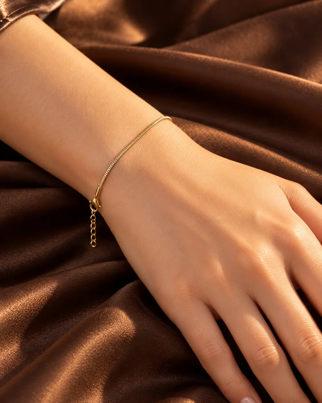 Wrist on brown satin wearing the thin gold snake chain bracelet