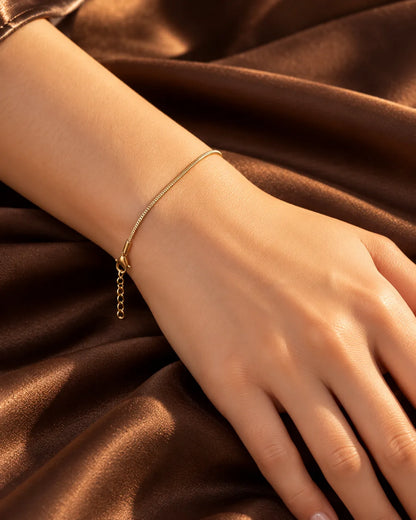 Wrist on brown satin wearing the thin gold snake chain bracelet
