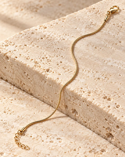 Gold snake chain bracelet draped over a stone block