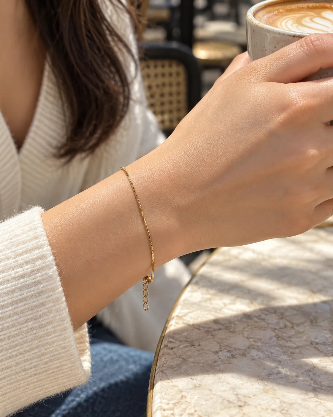 Wrist holding a coffee cup wearing the gold snake chain bracelet