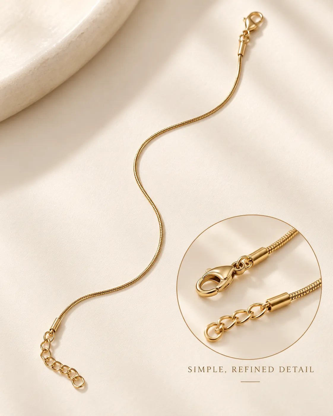 Gold snake chain bracelet on cream fabric with an inset of the clasp