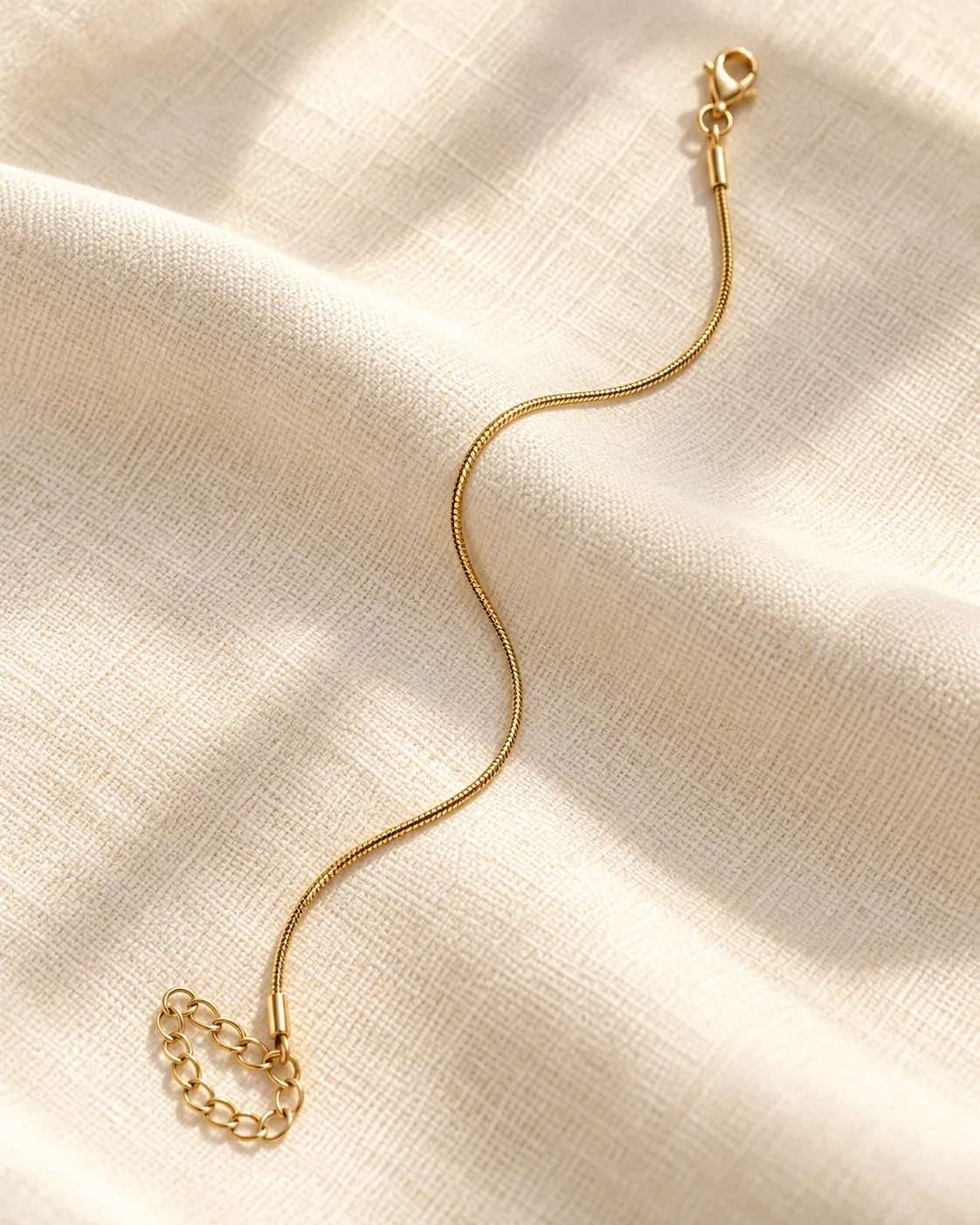 Minimal gold snake chain bracelet laid on cream fabric