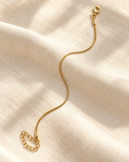 Minimal gold snake chain bracelet laid on cream fabric
