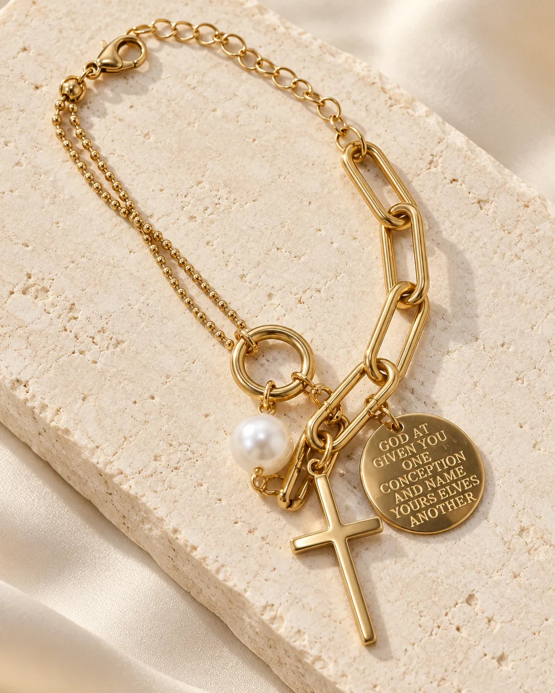 Gold cross charm bracelet displayed on a stone block