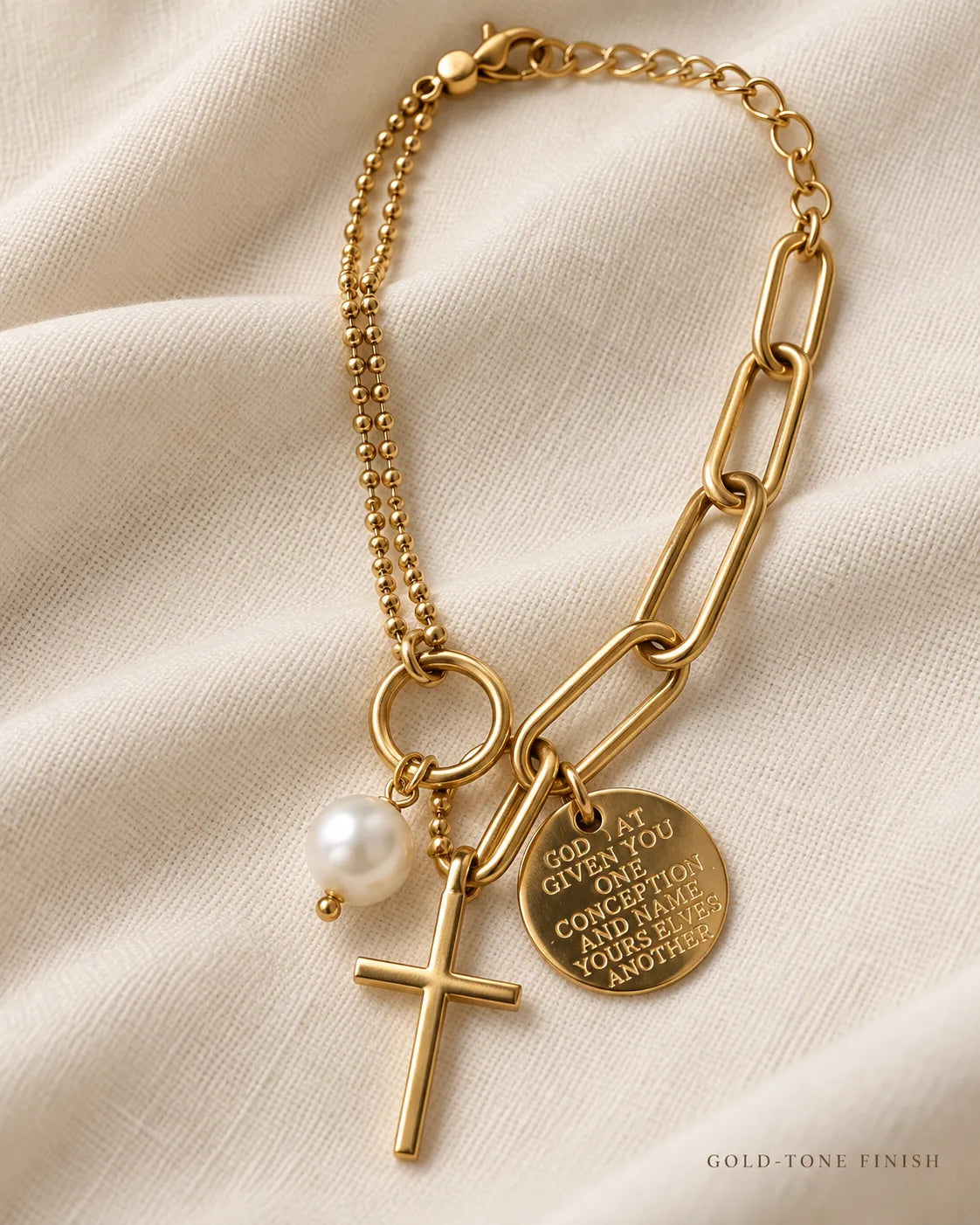 Gold double-chain cross bracelet laid on cream fabric