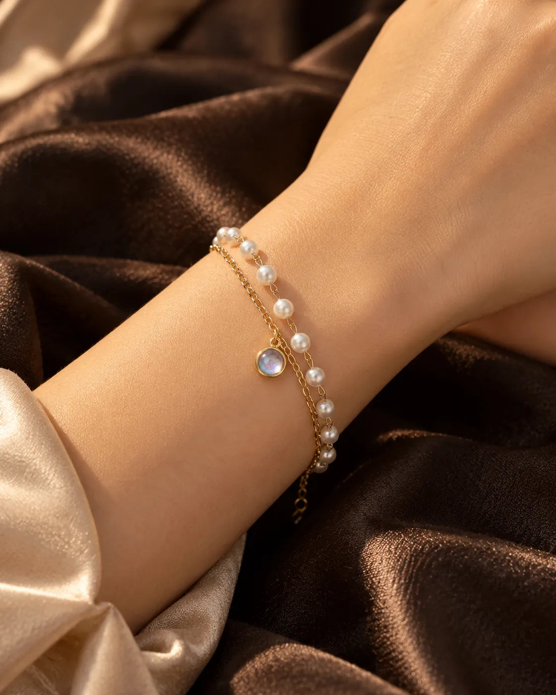 Wrist on brown satin wearing the gold chain and pearl-look bracelet