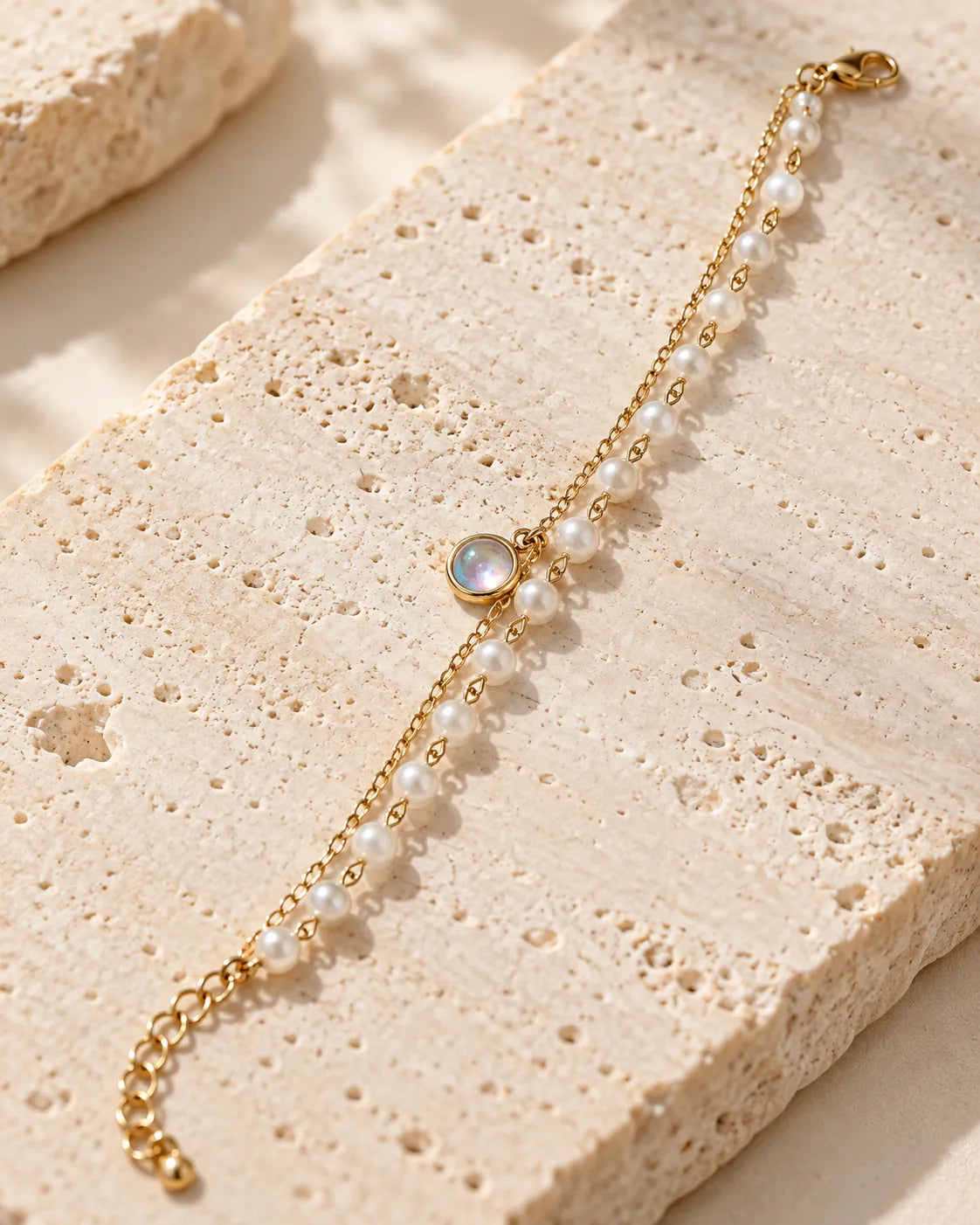 Gold chain and pearl-look double bracelet on a stone block