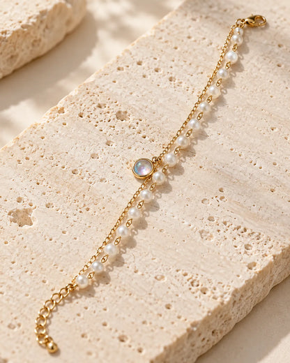 Gold chain and pearl-look double bracelet on a stone block