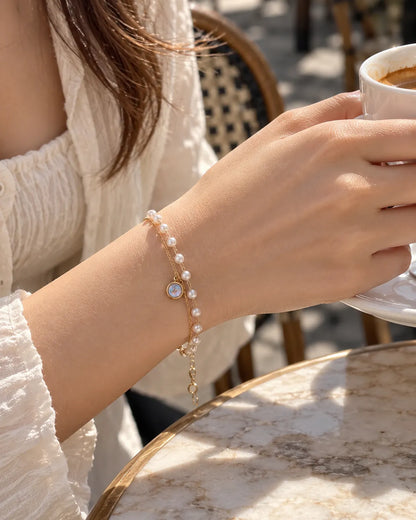 Wrist at a cafe wearing the gold and pearl-look double bracelet