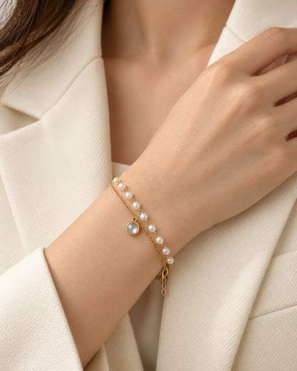 Wrist in a white blazer wearing the gold pearl-look double bracelet