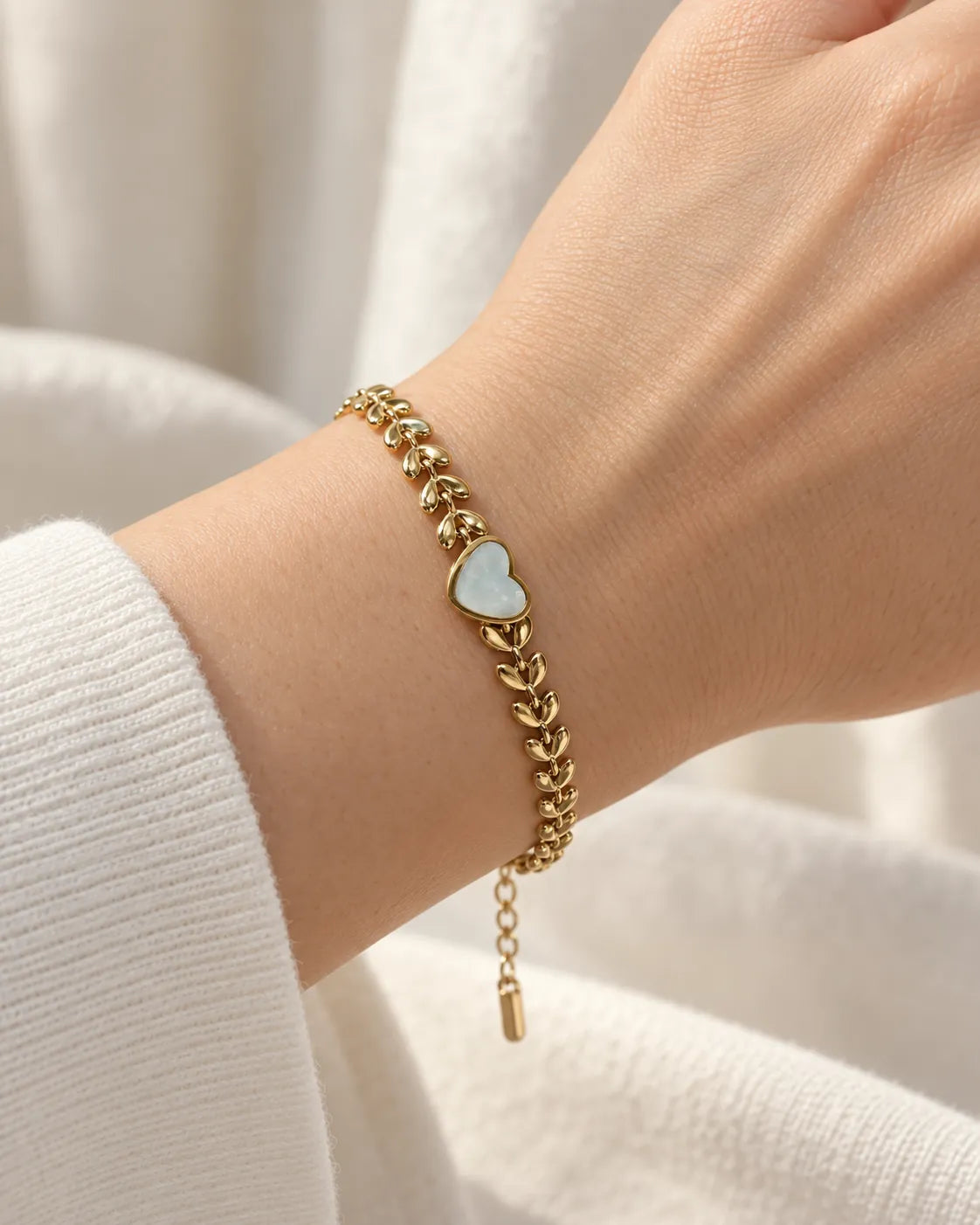 Wrist in a white sleeve wearing the gold leaf chain heart bracelet