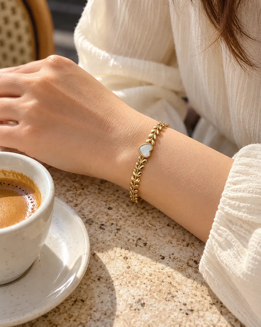 Wrist holding a coffee cup wearing the gold heart bracelet