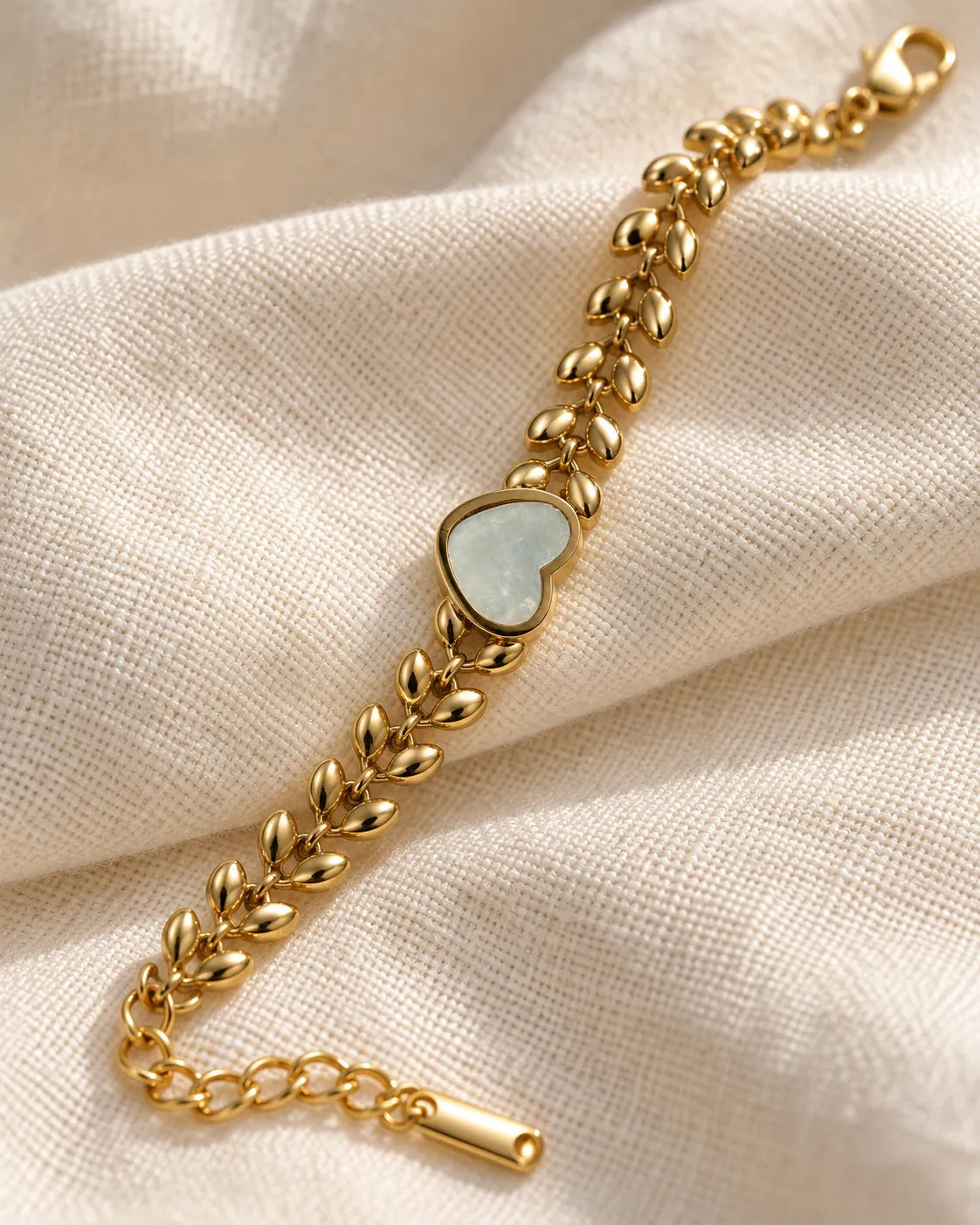 Gold leaf link bracelet with white heart laid on cream fabric