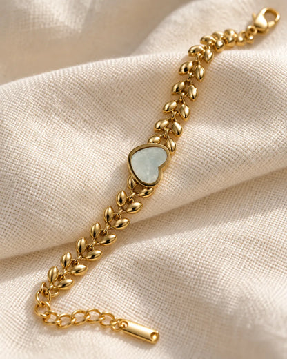 Gold leaf link bracelet with white heart laid on cream fabric