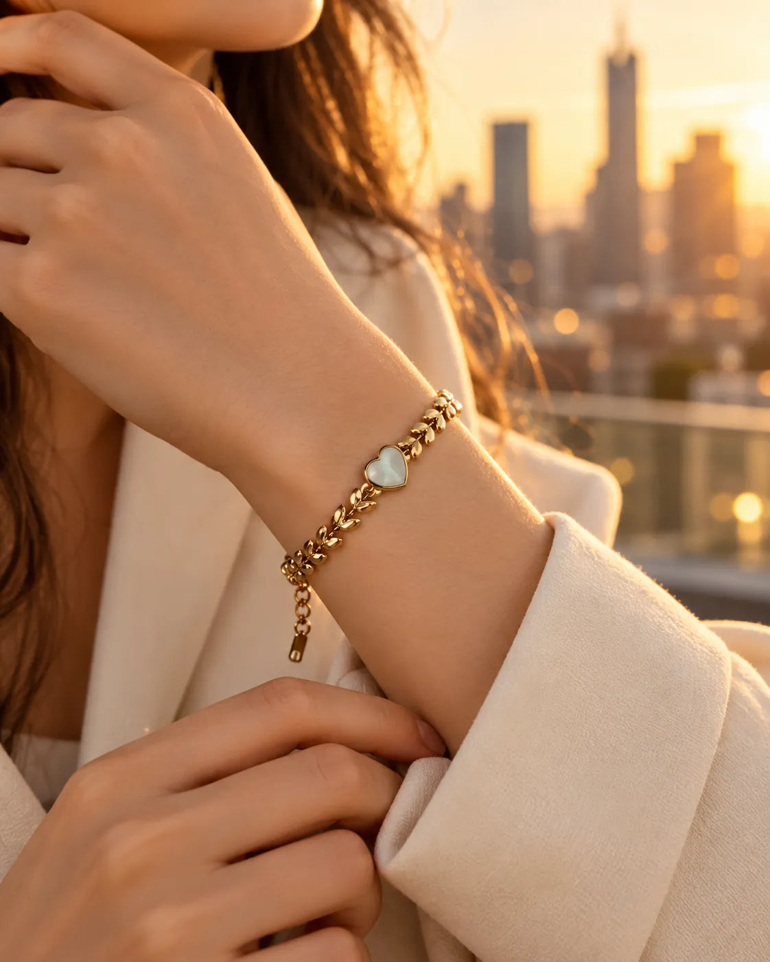 Wrist wearing the gold heart bracelet against a city skyline at sunset