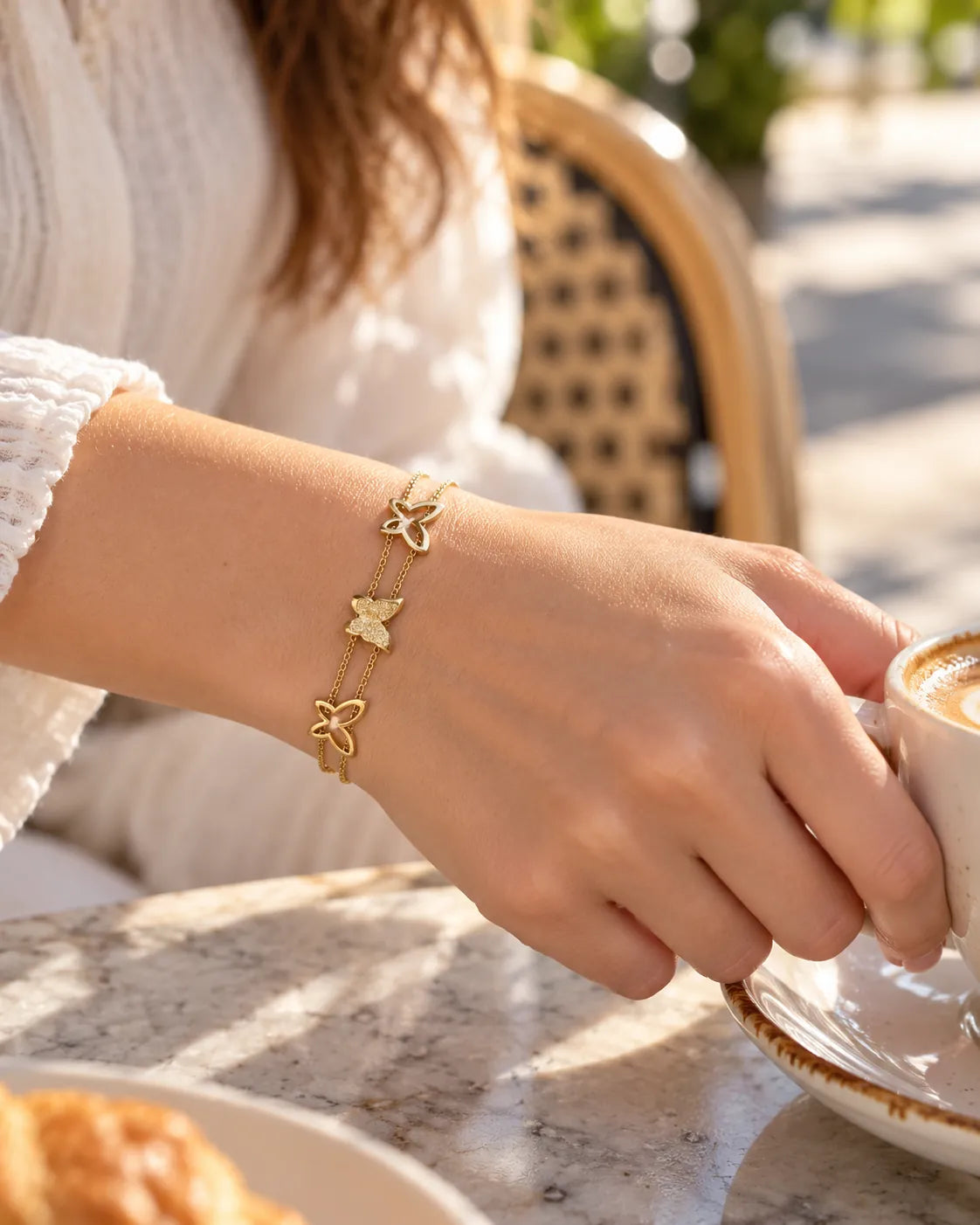 Wrist at a cafe wearing the gold double chain butterfly bracelet