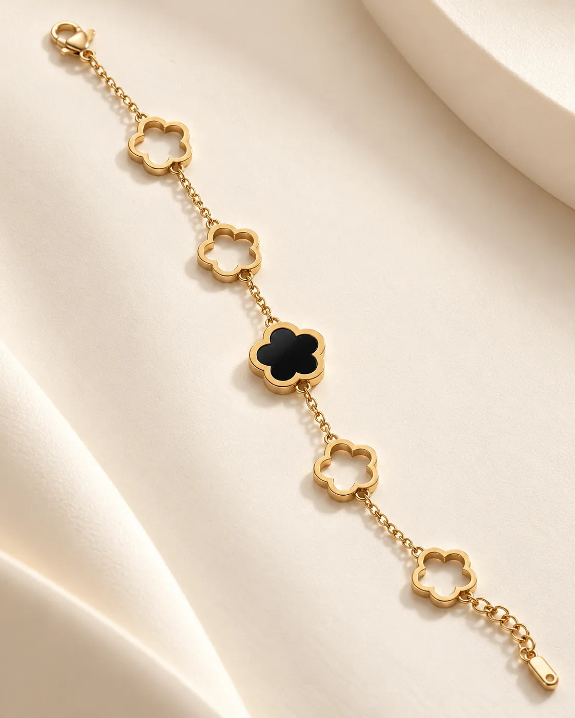 Gold chain bracelet with black clover flower and open flower links on cream fabric